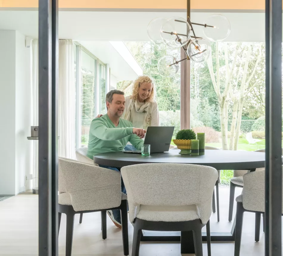 Een man en vrouw bekijken hun energiecontract in een warme woonkamer met groen op de achtergrond.